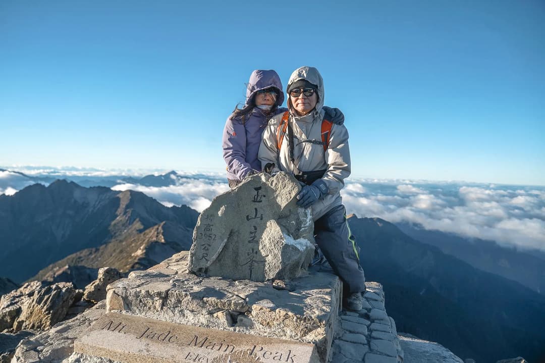 夫妻在玉山主峰3952公尺山頂碑前合影,背後是雲海